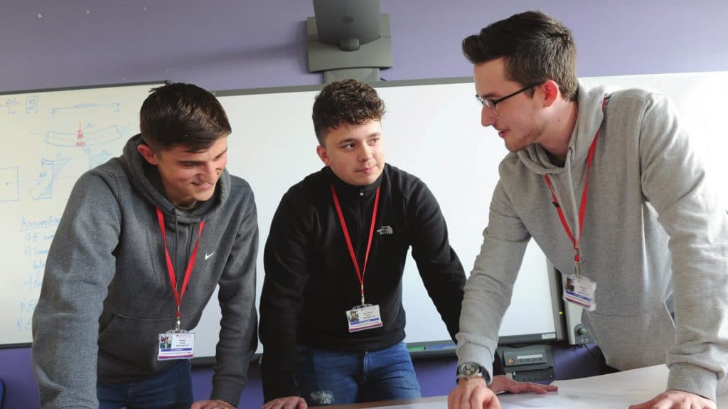 Three student collaborate at a classroom desk.