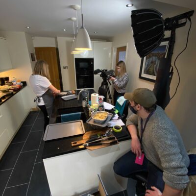 Dan working in a kitchen producing his first project, lighting, camera and a female actress are in the picture.