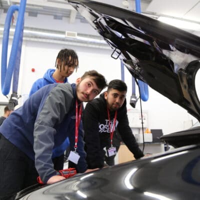 three students lean over a car engine