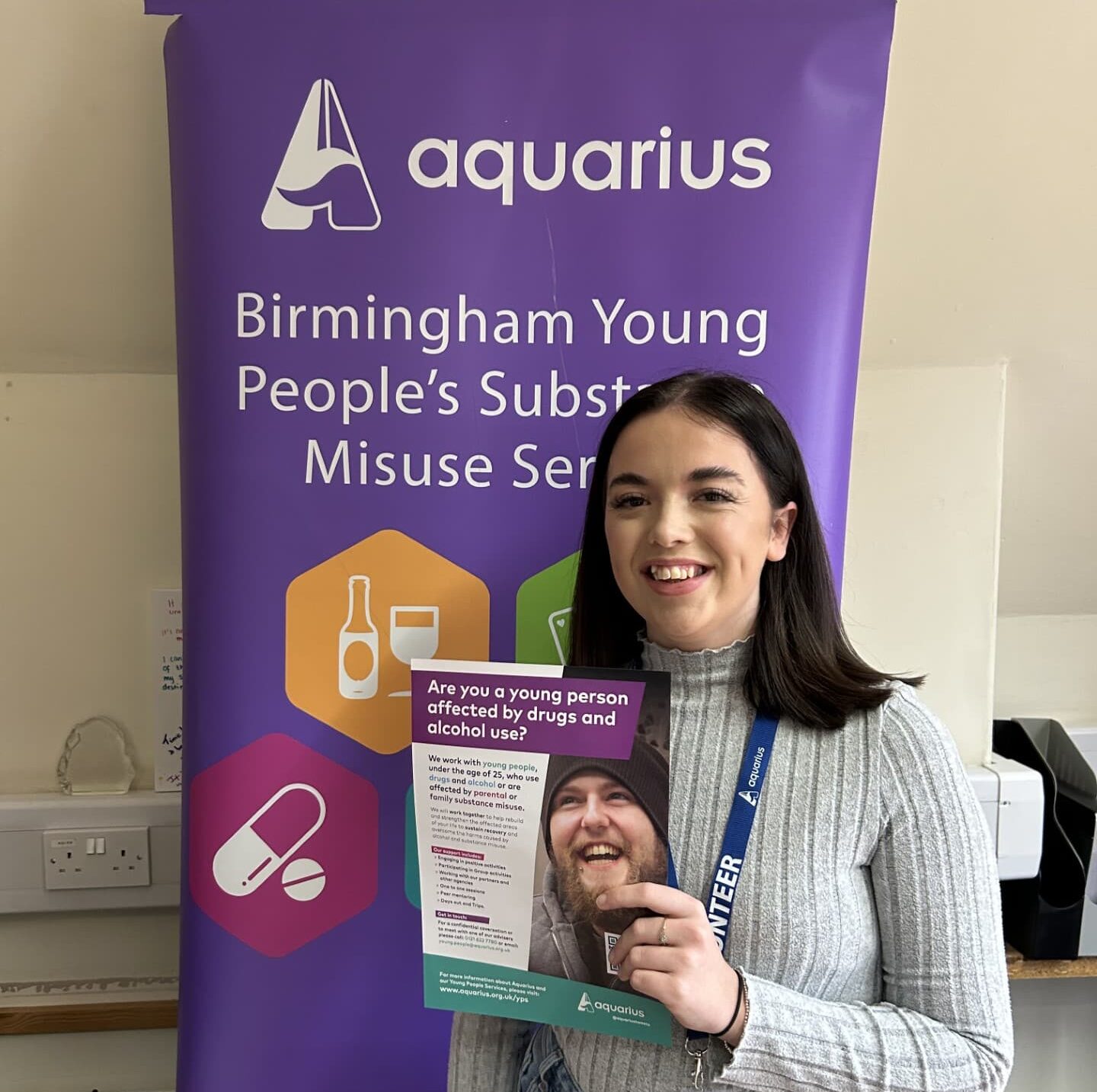 Holly Lewis posing in front of an Aquarius charity banner