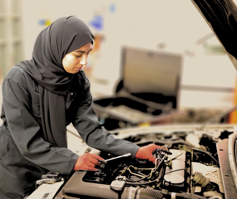 student looking at inside of the car and fixing it with tool