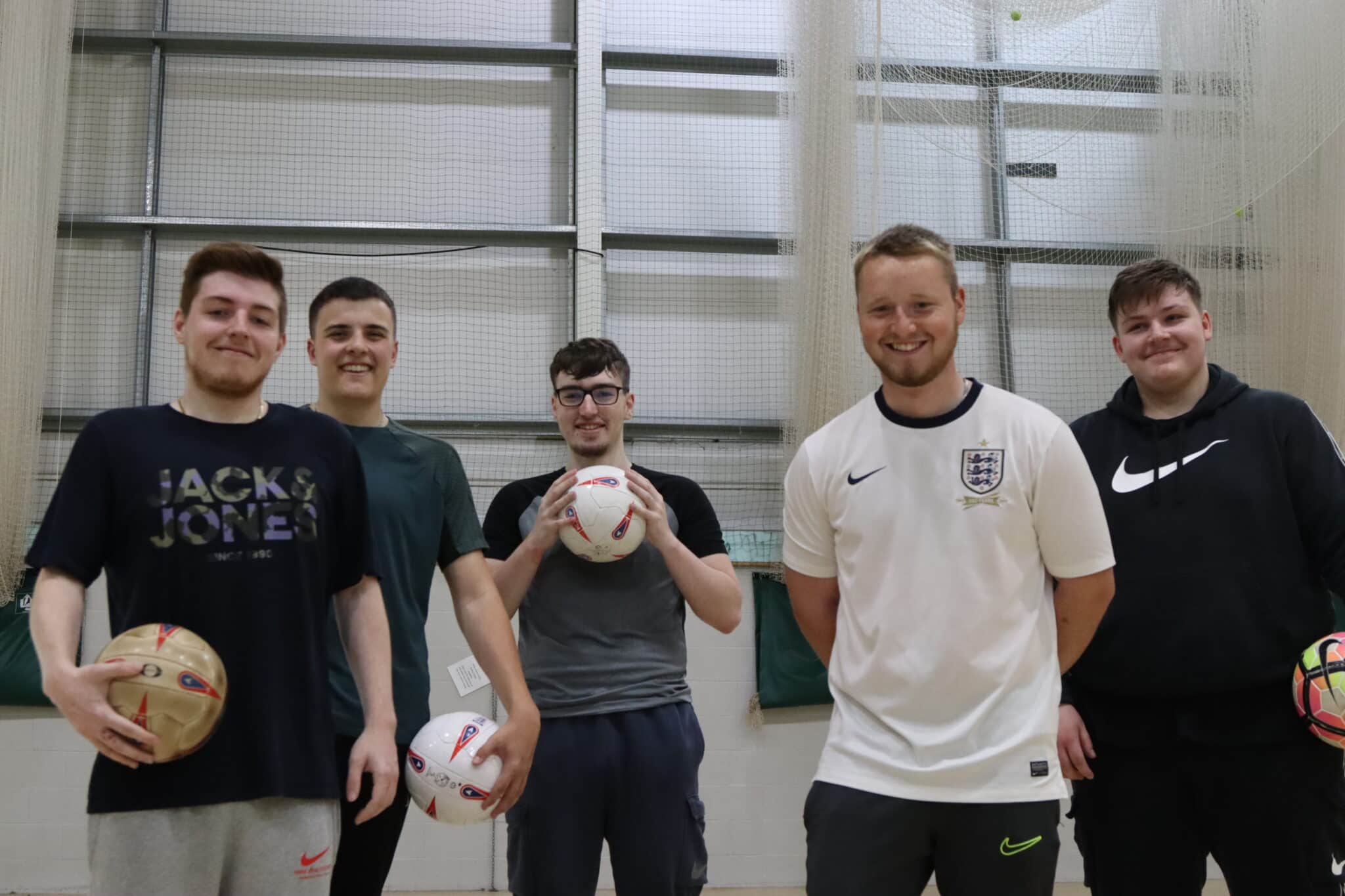 5 students standing in sports hall, three holding a football