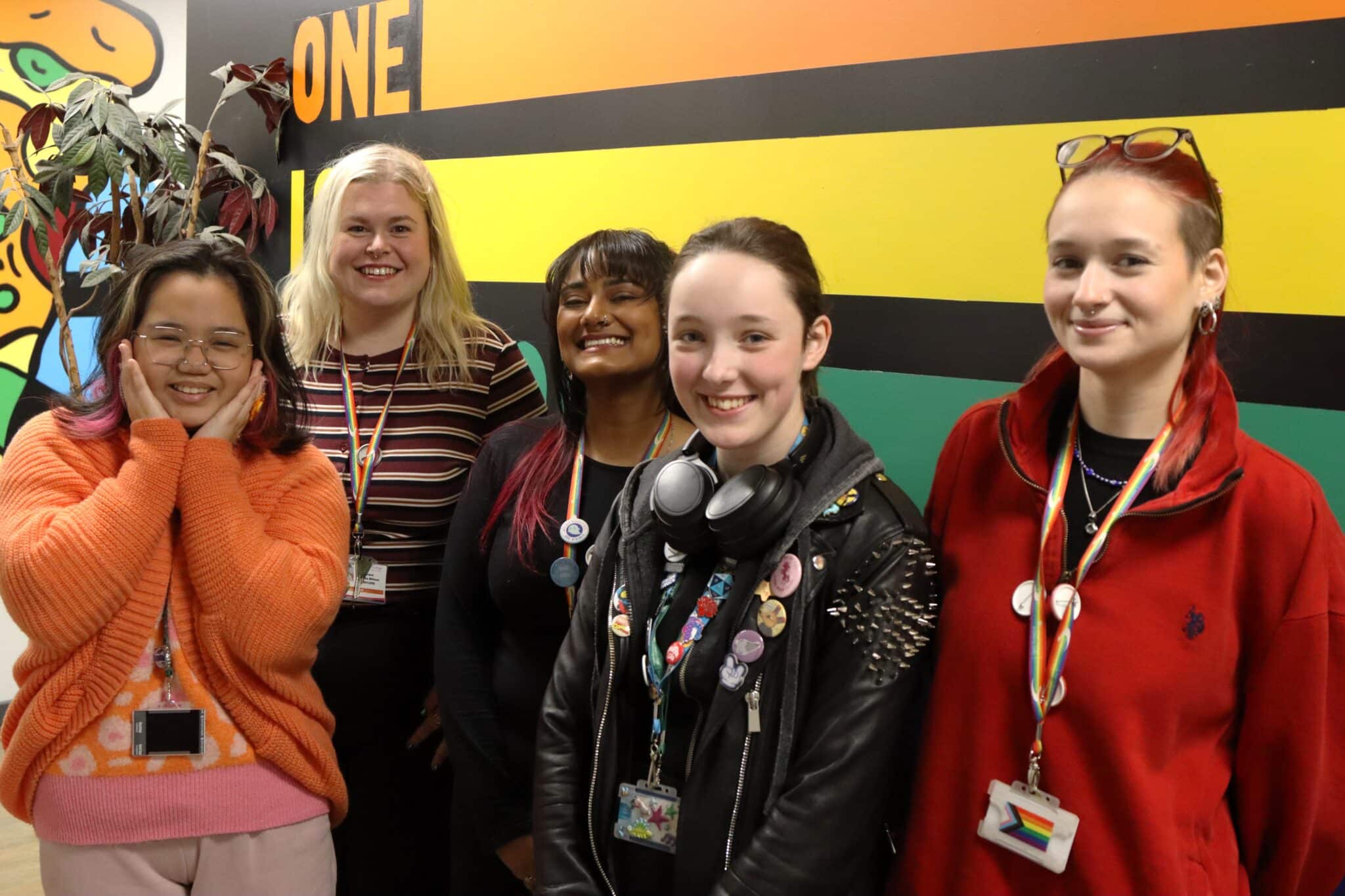 5 people standing in front of flag smiling at College prestigious Rainbow Flag Award