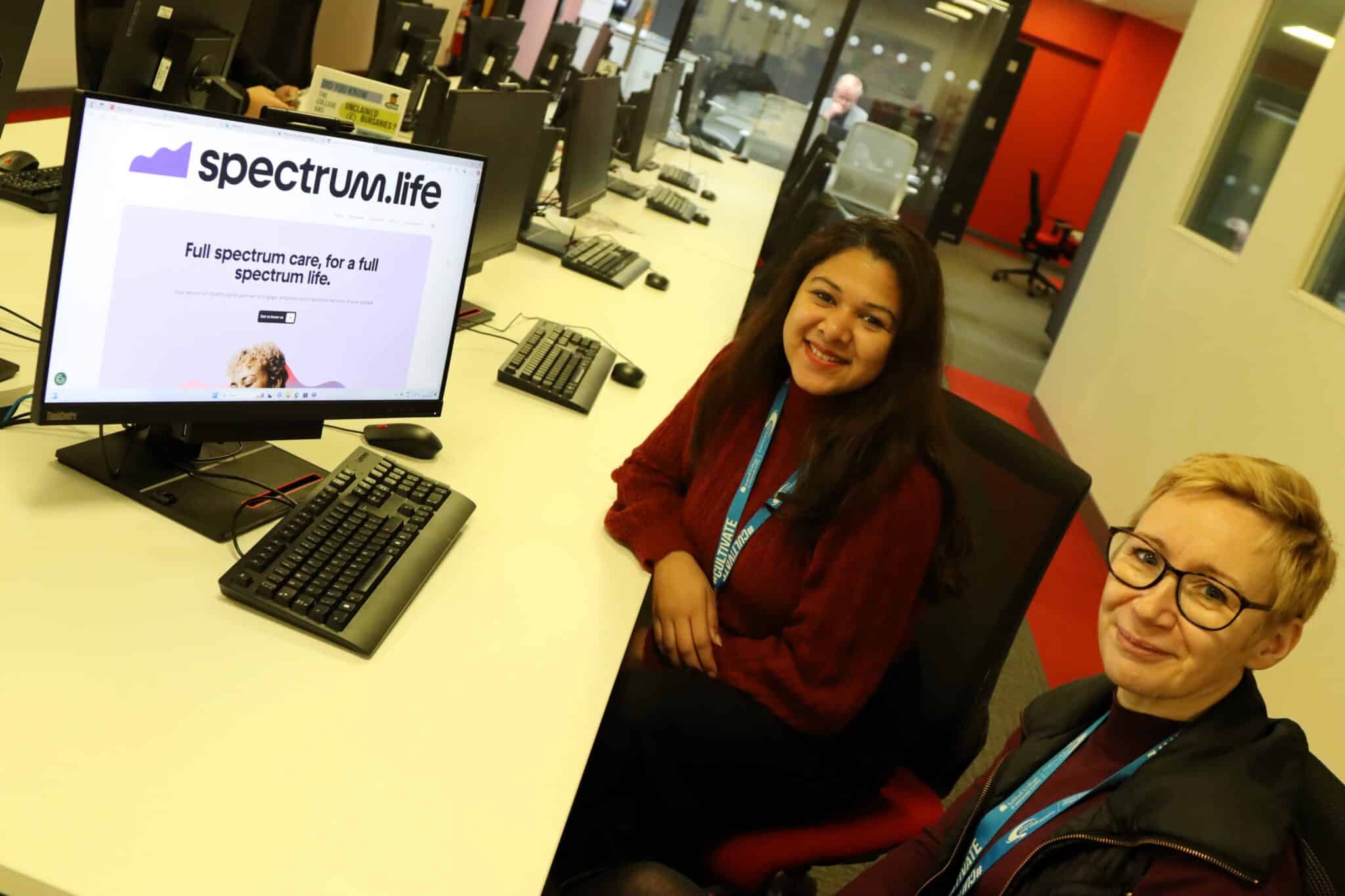 two Solihull College staff members looking up at camera sat next to computer screen