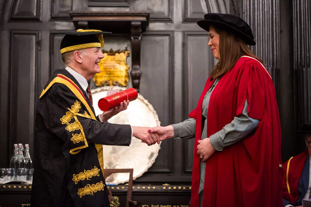 College Principal awarded prestigious Fellowship to Rebecca, who is shaking hands with him