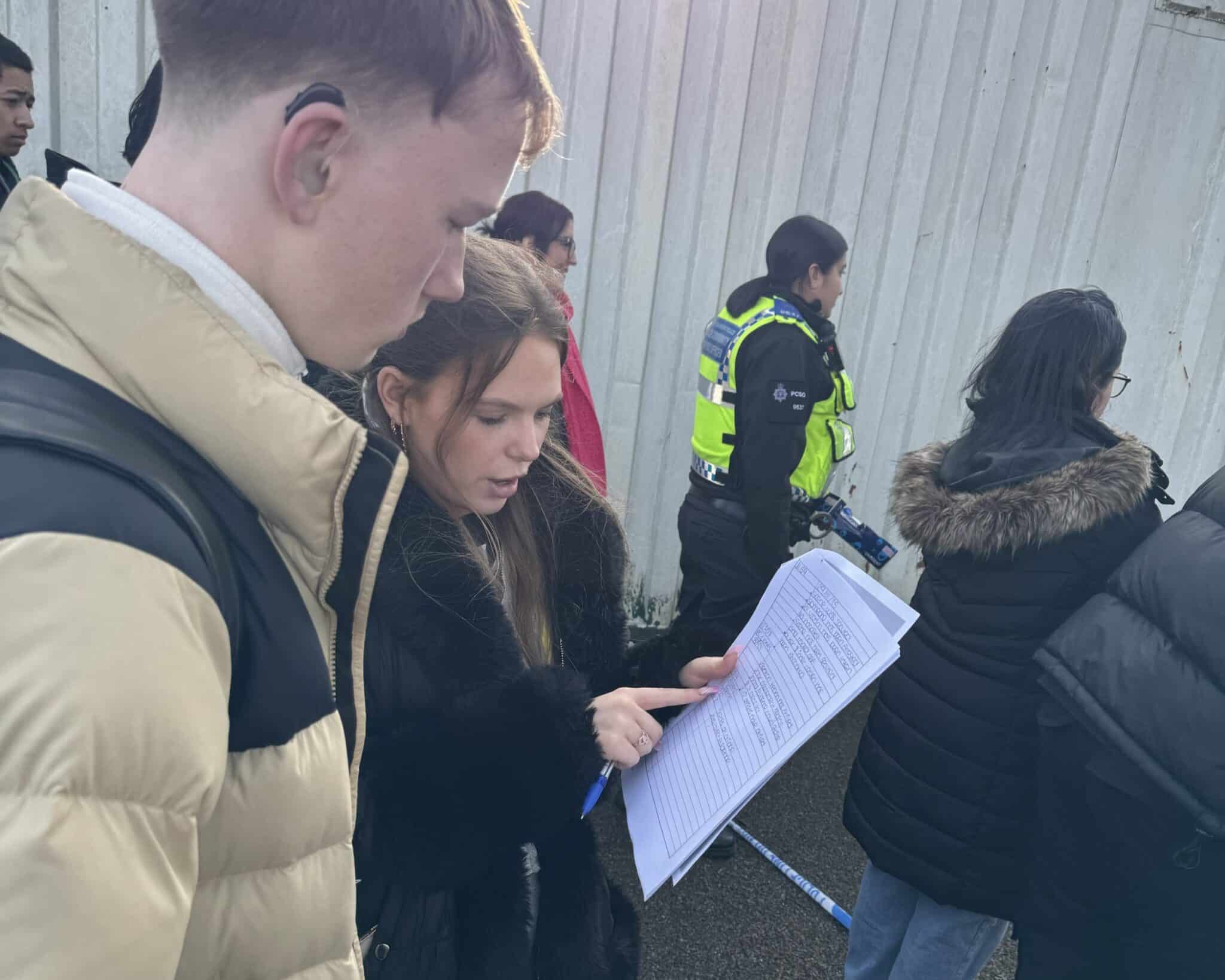 students studying paperwork with poiice in background